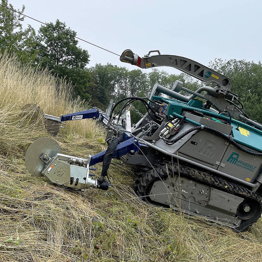 Ferngesteuerter Mäher auf schrägem Gelände, schneidet hohes Gras effizient. Robotertechnik für Landschaftspflege.