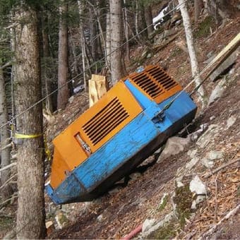 Orange-blaues Maschinengehäuse in einem Wald, an einem steilen Hang befestigt.