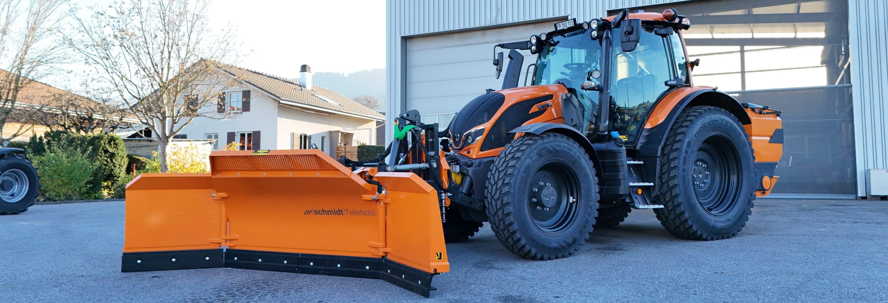 Traktor mit Schneepflug vor Gebäude, ideal für Wintereinsätze in landwirtschaftlichen und städtischen Gebieten.